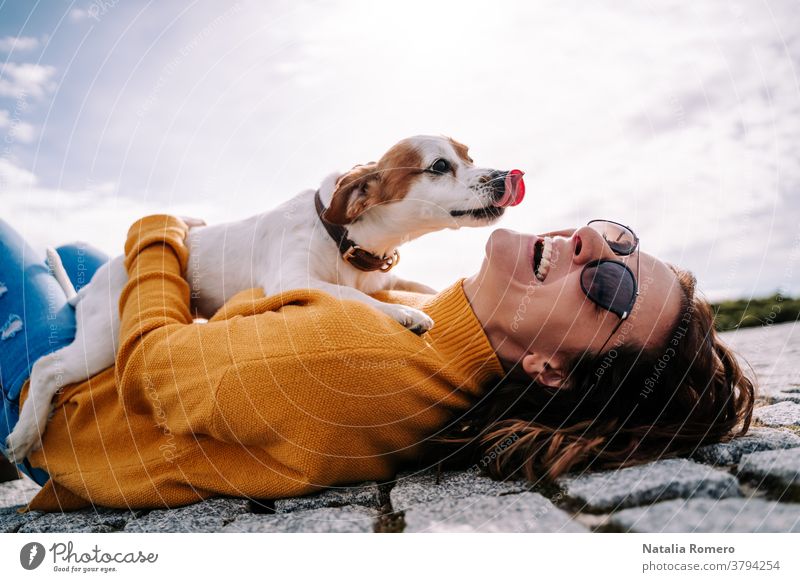 A beautiful woman laughing while her pet is licking her face in a sunny day in the park in Madrid. The dog is on its owner between her hands. Family dog outdoor lifestyle