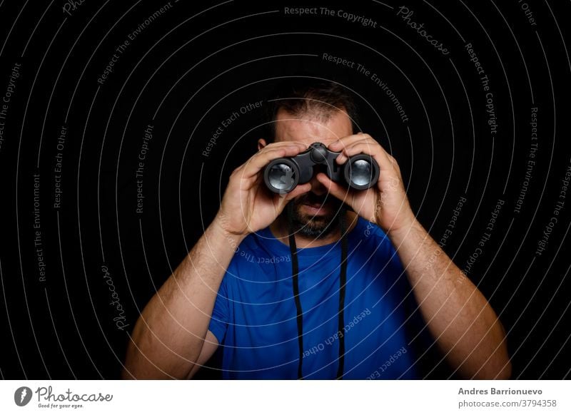 Bearded man dressed in blue t-shirt with binoculars posing against black background clothes sunglasses lifestyle happy handsome friendly studio shot posture