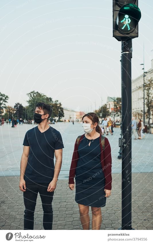 Man and woman waiting at pedestrian crossing next to traffic lights wearing the face masks to avoid virus infection and to prevent the spread of disease in time of coronavirus