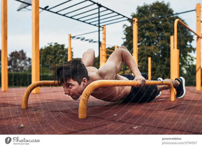 Young shirtless man bodybuilder doing push-ups on a parallel bars during his workout in a modern calisthenics park care caucasian health lifestyle male one