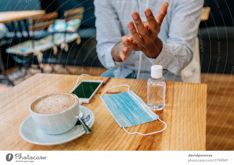 Unrecognizable man disinfecting his hands with hydroalcoholic gel disinfecting hands coronavirus hand rub rubbing applying mask on table coffee shop