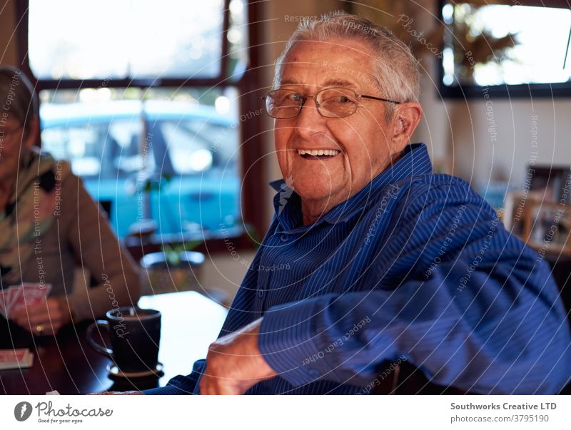 Portrait Of Smiling Senior Couple At Home Sitting At Table Playing Cards Together couple senior seniors retired at home playing cards game card game hobby