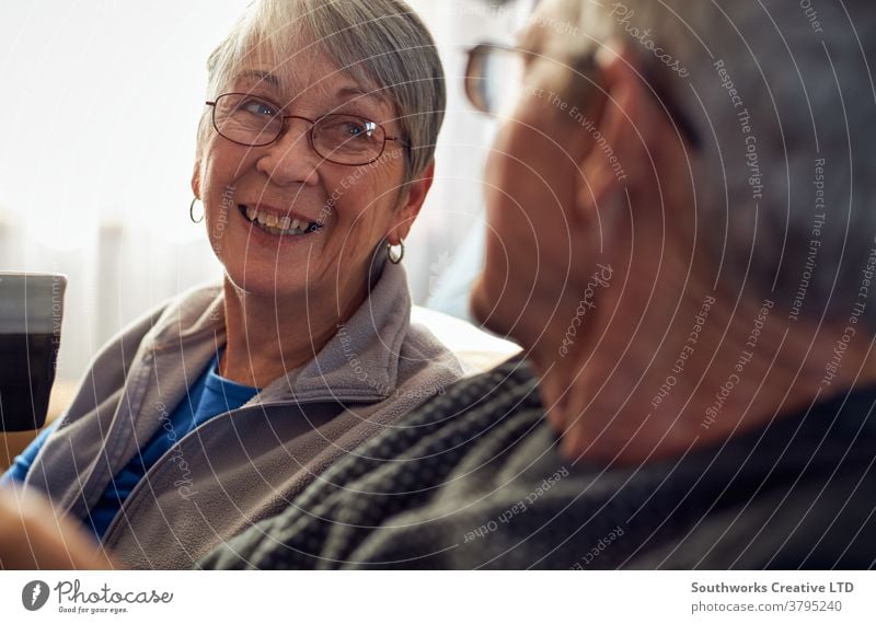 Senior Couple Relaxing And Chatting On Sofa At Home Together couple senior seniors retired at home relaxing sitting sofa talking chatting indoors happy smiling