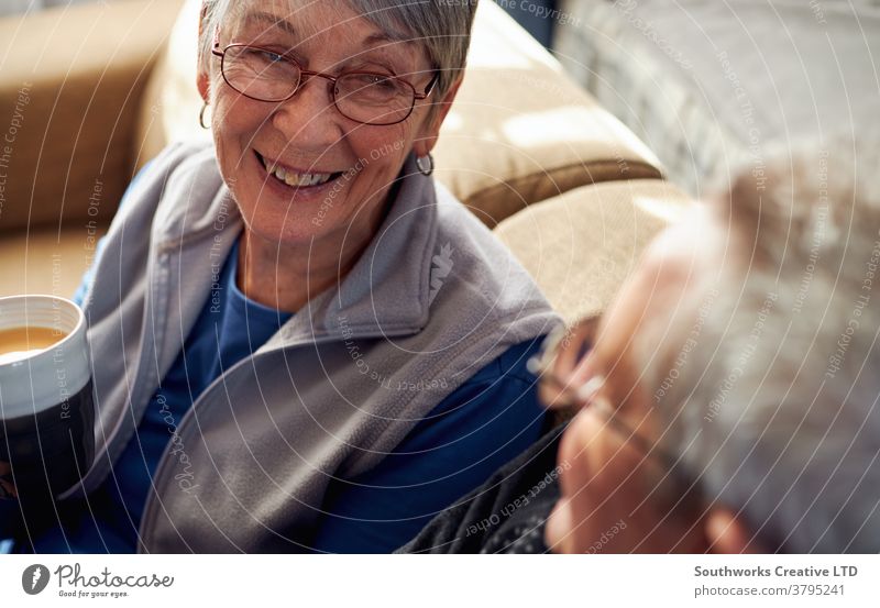 Senior Couple Relaxing And Chatting On Sofa At Home Together With Hot Drink couple senior seniors retired at home relaxing sitting sofa talking chatting drink