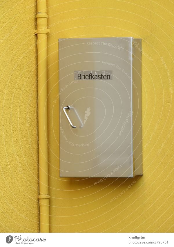 Silver-coloured mailbox on a yellow house wall with yellow downpipe Mailbox Box safekeeping Exterior shot Metal Day Colour photo Deserted Wall (building)