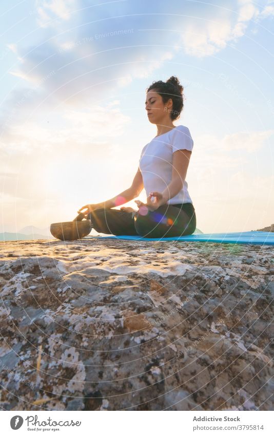 Relaxed woman meditating on mountain top yoga meditate lotus pose balance zen serene peaceful nature sit asana padmasana mudra rock practice position tranquil