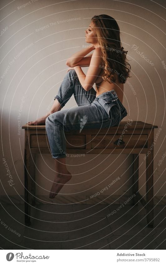 Stylish sensual model on table near wall denim reflective eyes closed topless seductive appearance hairstyle barefoot wear mindfulness woman dreamy feminine