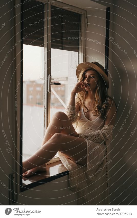 Sensual pondering woman in stylish apparel on windowsill sensual feminine sensitive melancholy home straw hat trendy modern style wistful barefoot rest