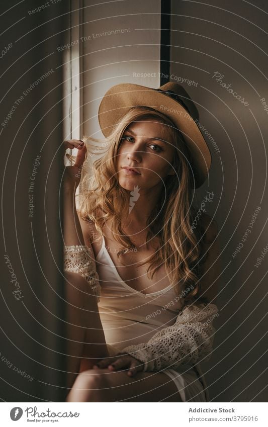 Sensual pondering woman in stylish apparel on windowsill sensual feminine sensitive melancholy home straw hat trendy modern style wistful barefoot rest