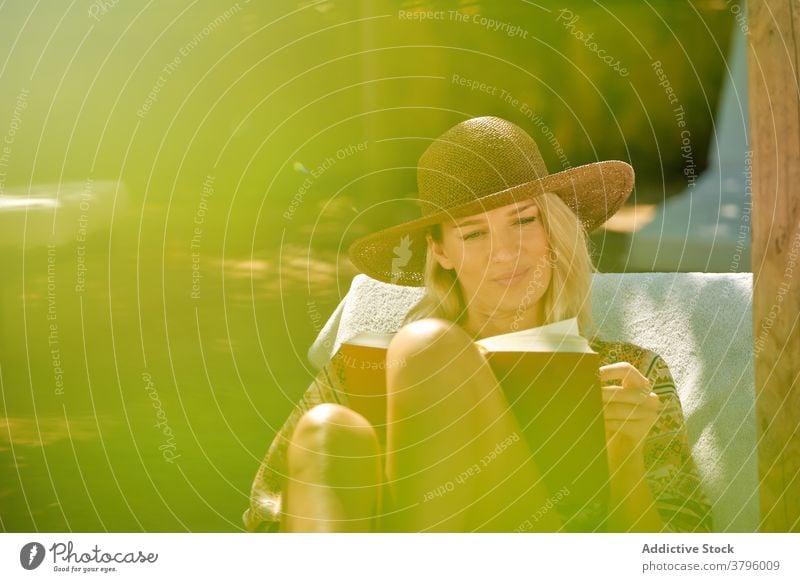 Cheerful female tourist reading book while resting on deckchair woman chill toothy smile beautiful travel happy holiday relax resort lounge break vacation