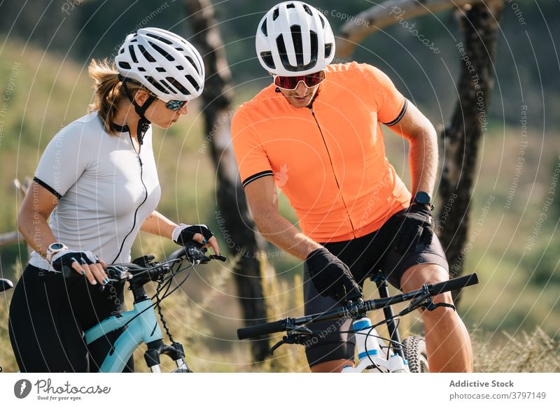 Cheerful cyclists standing on hill in mountains couple bicyclist together sport helmet professional bicycle bike relax break rest interact nature healthy