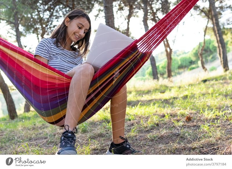 Smiling woman in hammock with laptop freelance project using typing startup independent cheerful female young internet gadget device netbook browsing lying work