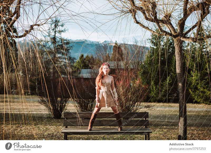 Trendy woman in fashionable outfit standing on bench in highlands style dress garment nature mountain countryside trendy young female spring elegant glamour