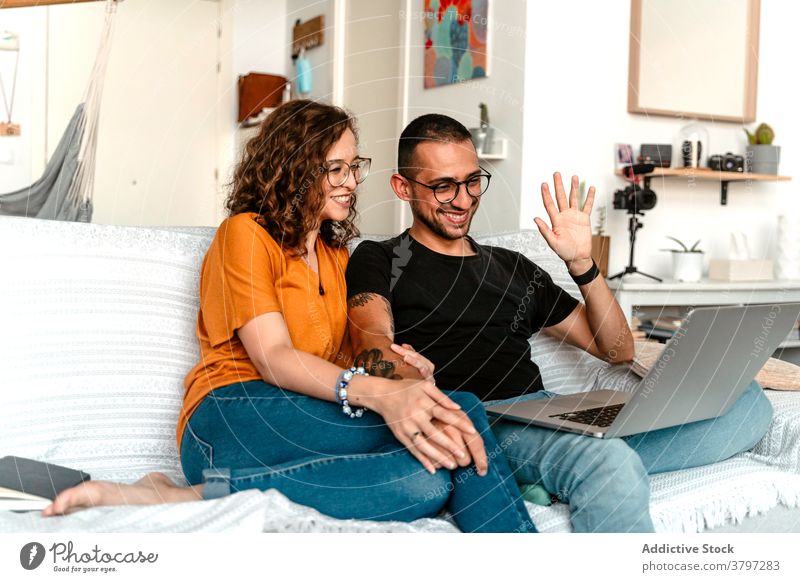 Happy couple having video conversation on laptop at home video call happy together holding hands sofa wave hand cheerful connection relationship boyfriend