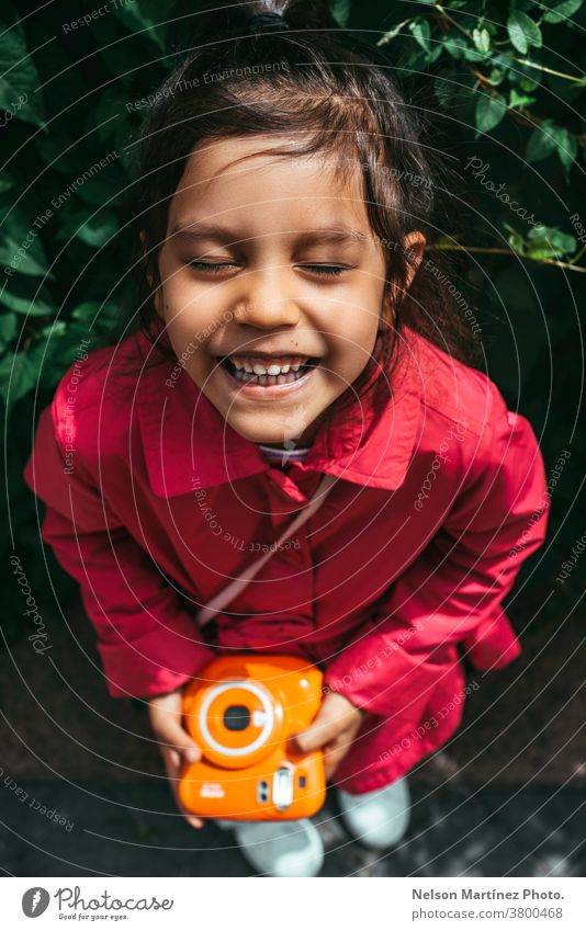 Portrait of a cute hispanic kid wearing a fuchsia jacket. She is holding a polaroid camera in her hands. smiling photography vintage instax latin Human being