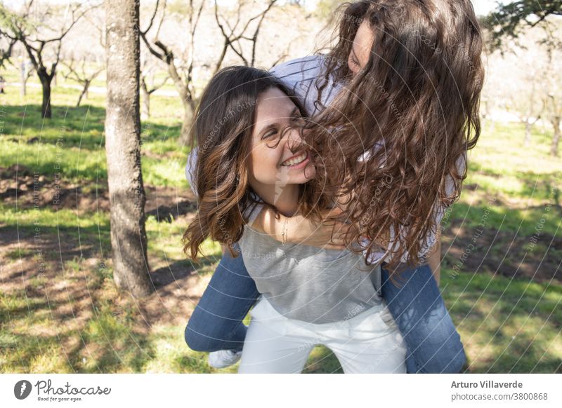 two girls a park of almond trees laughing together, climbed one on top of the other activity background beautiful bright careless cheerful colorful female