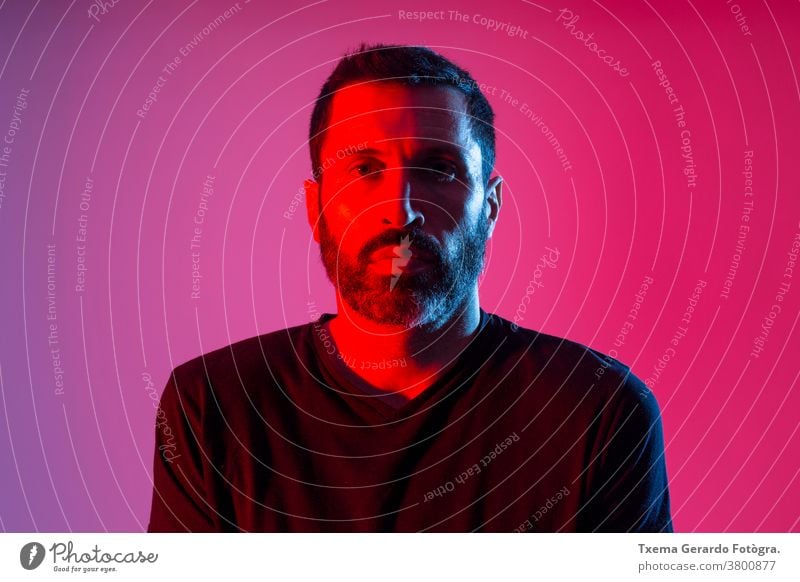 Colorful studio portrait of a bearded man against red and blue background. facial expression colored front view colorful dark sweatshirt art model adult face