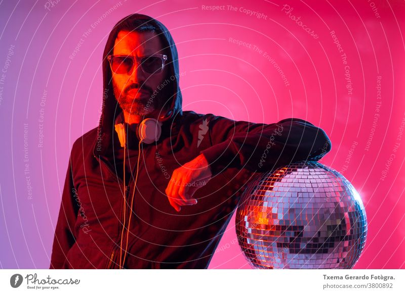 Colorful studio portrait of a bearded deejay with headphones and sunglasses against red and blues background. disco music colored pop sound disco ball mirrors