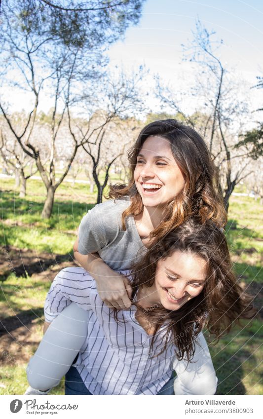 two girls a park of almond trees laughing together, climbed one on top of the other activity background beautiful bright careless cheerful colorful female