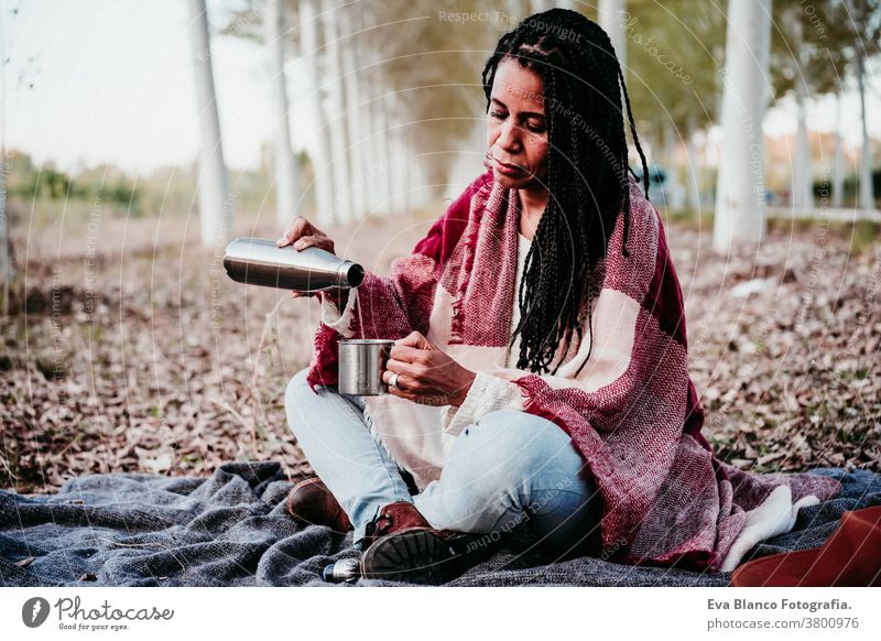 hispanic mid adult woman outdoors pouring water from a thermos. Autumn season afro woman latin portrait sunset nature hat smile happy joy young happiness people