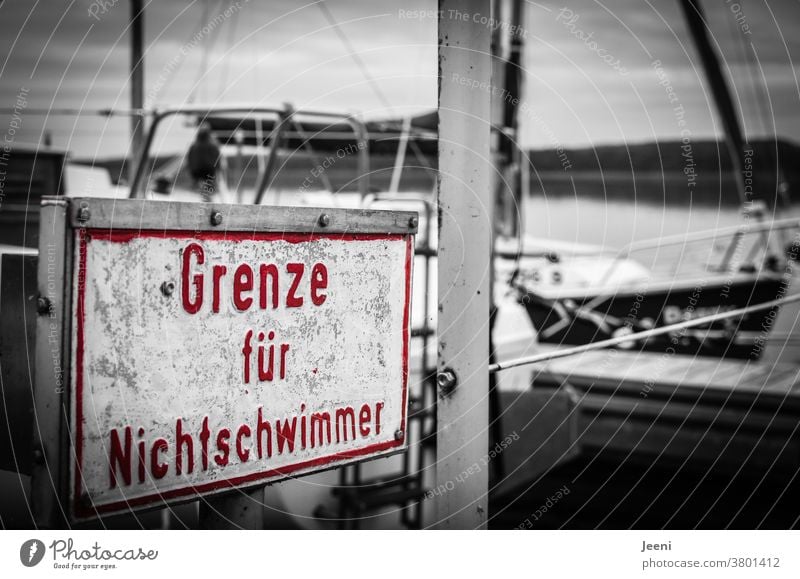 On a jetty at the lake there is a sign in the colour red with the inscription "Limit for non-swimmers Non-swimmer Border Water Rescue Drown First Aid Lifeguard