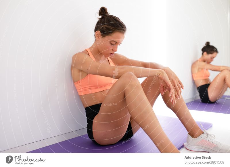 Tired sportswoman resting on mat after working out in gym tired eyes closed sportswear break mirror reflection exhausted fit white wall sit sneakers modern