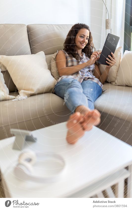 Cheerful woman browsing tablet in living room relax home entertain using message domestic weekend female internet connection social media happy device sofa