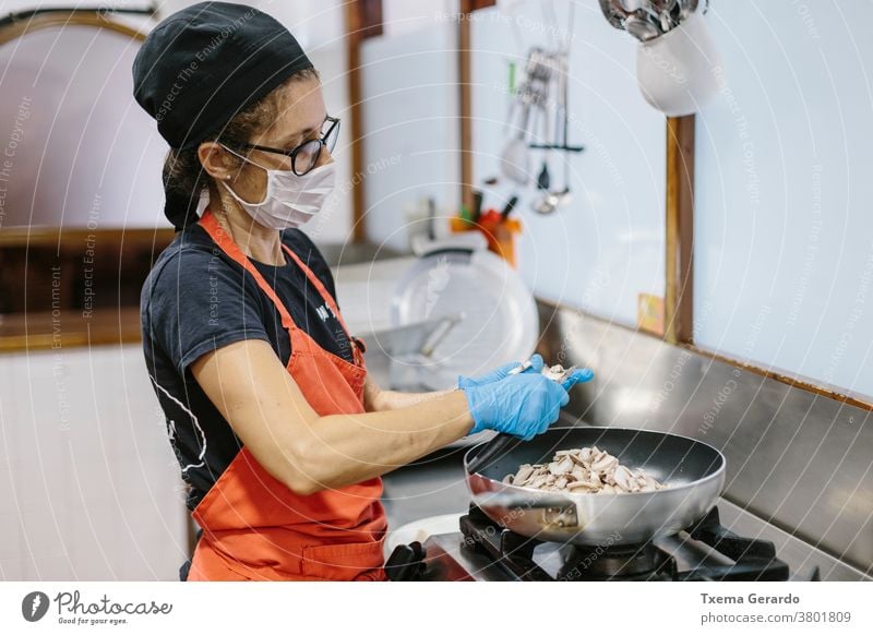 A cook in a restaurant wearing a mask as a precaution against the coronavirus preparing the meal. kitchen covid-19 cooking vegan vegetarian mushrooms frying pan