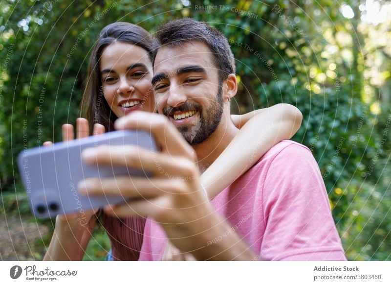 Cheerful ethnic couple taking selfie in park happy smartphone cuddle date romantic love together relationship gadget mobile girlfriend boy young casual embrace