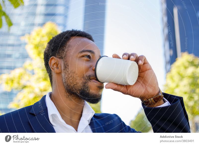 Bearded young black businessman drinking coffee in downtown street positive confident style beverage coffee break city sunlight urban male african american