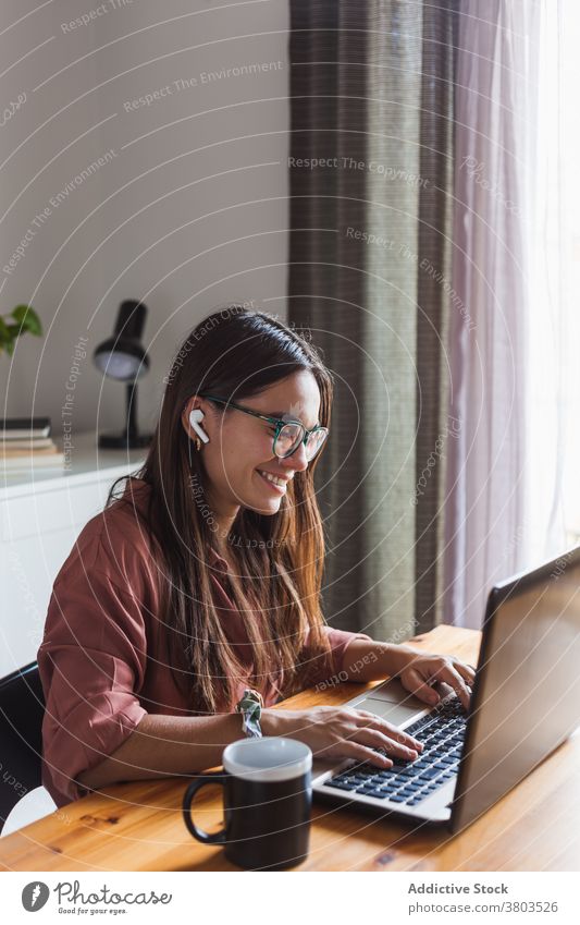 Smiling woman in earbuds typing on laptop at home workplace netbook happy browsing toothy smile satisfied using cheerful smart surfing gadget contemporary