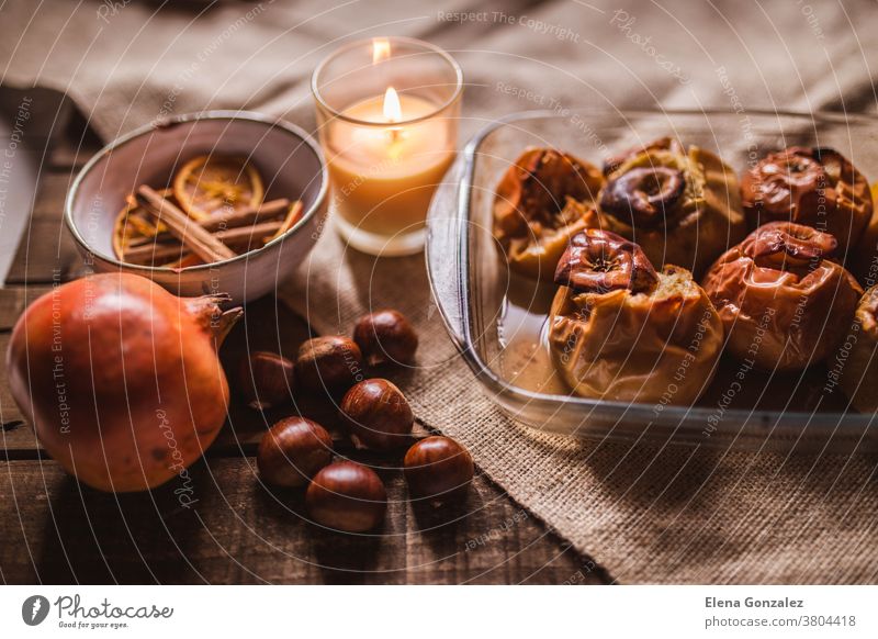 Roasted apples in a glass tray with chestnuts, candle, cinnamon, orange and pomegranate homemade cooking chili sugar vegetarian gourmet food sweet spoon natural