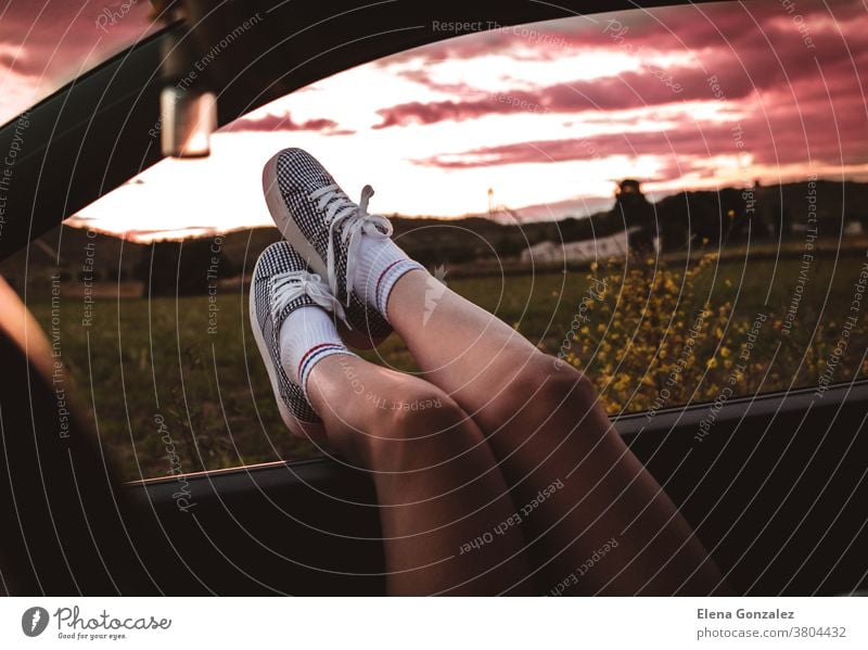 young woman with sneakers with feet propped on the car window at sunset legs journey people lifestyle sunlight road trip footwear travel fun girl tourist child