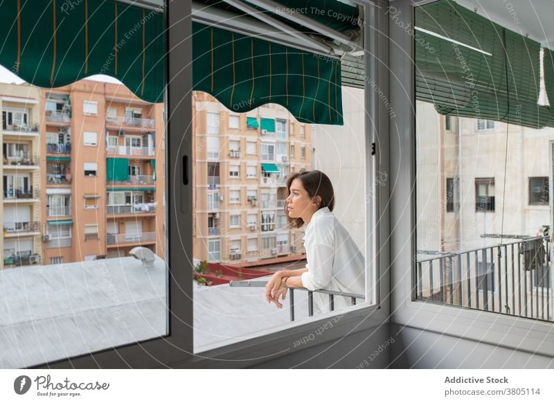 Calm young female on balcony of home woman morning calm enjoy relax rest terrace casual white shirt pensive dreamy recreation brunette sunlight peaceful