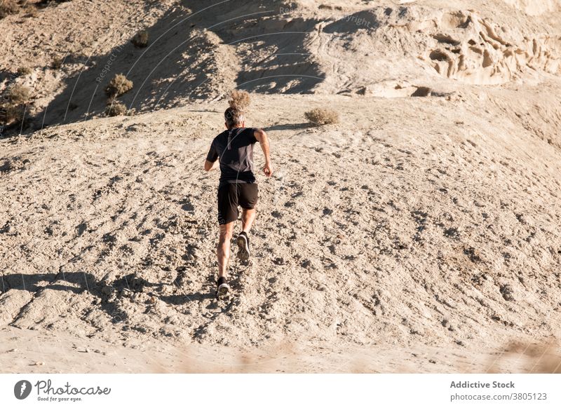 Anonymous sportsman jogging on sandy terrain in mountainous terrain run semi desert hill training active jogger healthy nature wellbeing exercise workout male