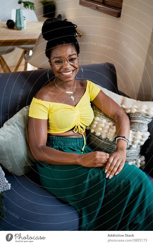 Cheerful black woman resting in living room toothy smile happy at home style fashion weekend free time sofa female african american eyeglasses apartment flat