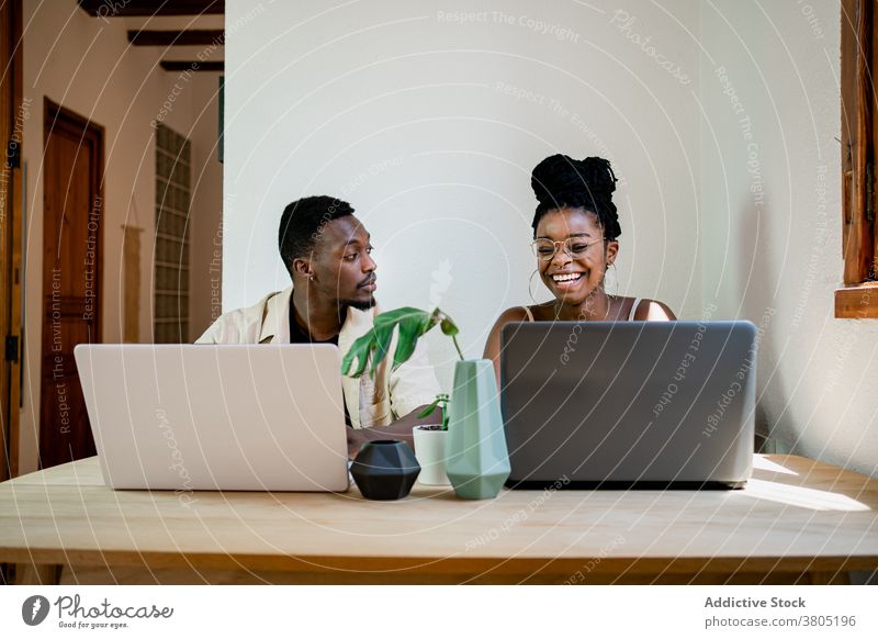 Cheerful young black couple working remotely on laptops at home positive point at camera together relationship cuddle cheerful job busy boyfriend girlfriend