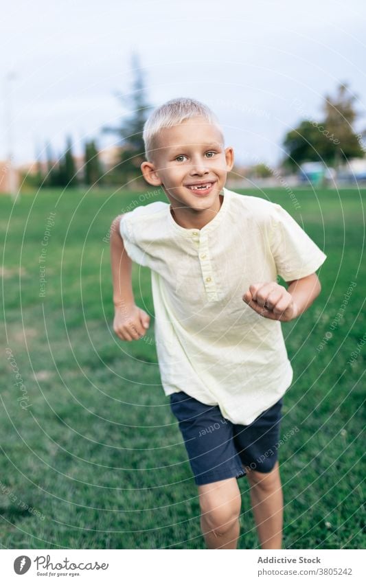 Cheerful boy running through park activity toothy smile positive cheerful weekend play game sport lawn grass nature carefree content delight pleasure enjoy