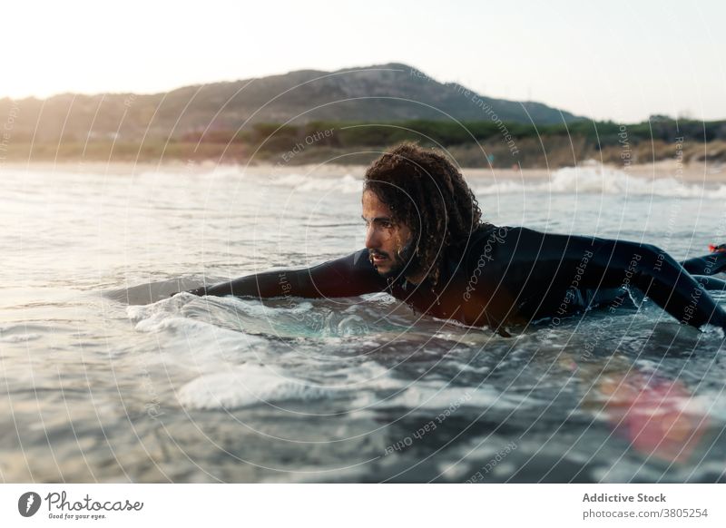 Concentrated surfer looking at coming wave man sea ocean water sports summer focus leisure surfboard male serious pensive curly hair wetsuit vacation beach