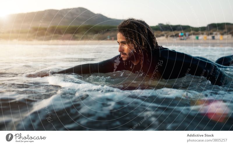 Concentrated surfer looking at coming wave man sea ocean water sports summer focus leisure surfboard male serious pensive curly hair wetsuit vacation beach