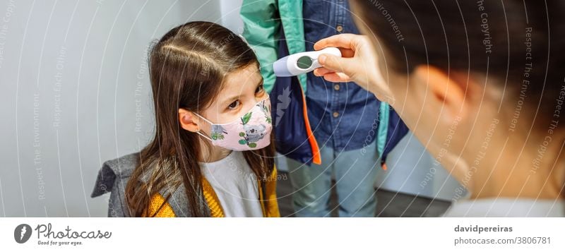 Mother checking her daughter's temperature before going to school mother non-contact thermometer face mask coronavirus before going school top view