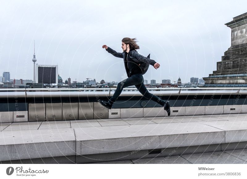 The dynamic young man jumps or hovers over Berlin with big steps panorama Reichstag Bundestag dome Roof Above Tall Man younger Dynamic Elated Spirited Jump far