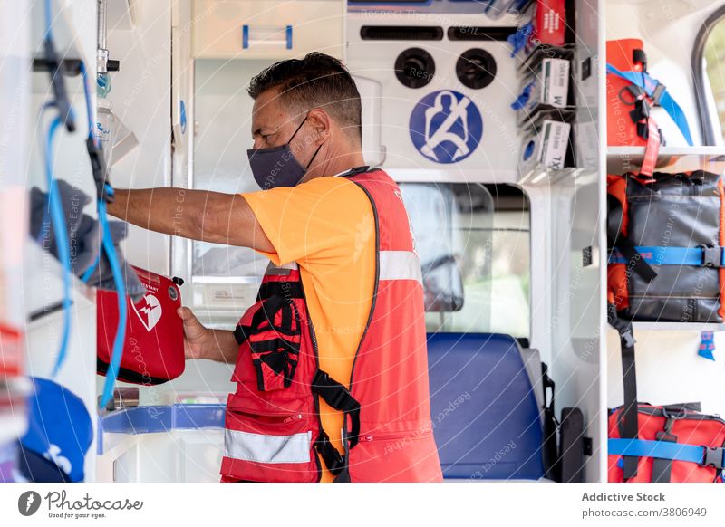 Anonymous worker in mask and uniform in ambulance car first aid kit professional equipment covid 19 protect employee bright job man service prevent stripe