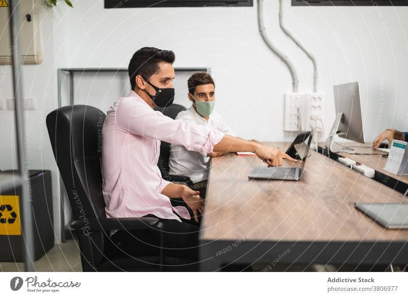 Unrecognizable colleagues in masks working on laptop at work entrepreneur share brainstorm startup internet office using device gadget men covid 19 tablet