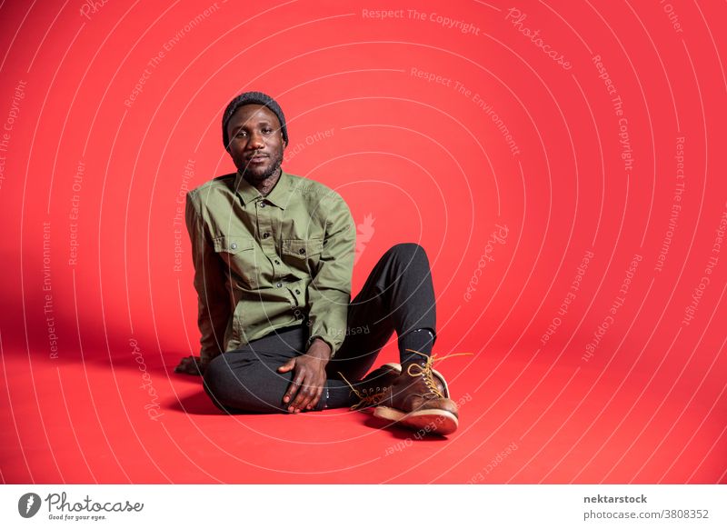 Young Black Man Posing Seated on Studio Floor man sit black content pose African ethnicity one person male one man only 20-30 years old handsome studio shot