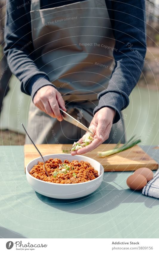 Crop chef cooking lunch in village on sunny day rustic man countryside mince meat add onion male apron table yard fresh cuisine meal green bowl appetizing