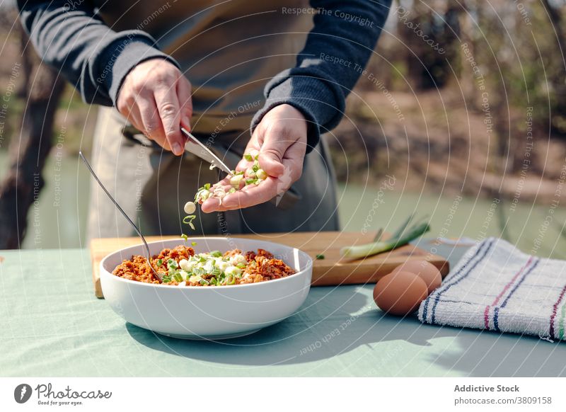 Crop chef cooking lunch in village on sunny day rustic man countryside mince meat add onion male apron table yard fresh cuisine meal green bowl appetizing