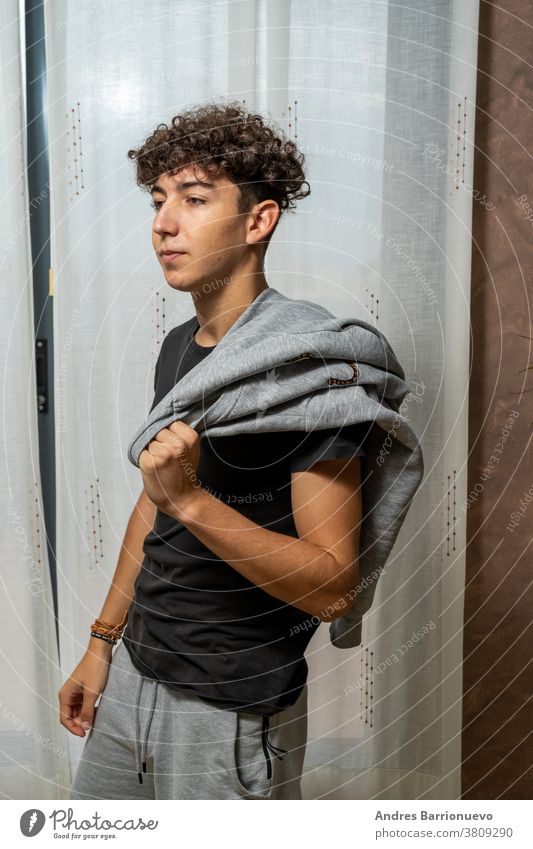 Attractive young man with curly hair wearing black t-shirt posing on white curtains background cheerful casual smile male adult handsome happy attractive