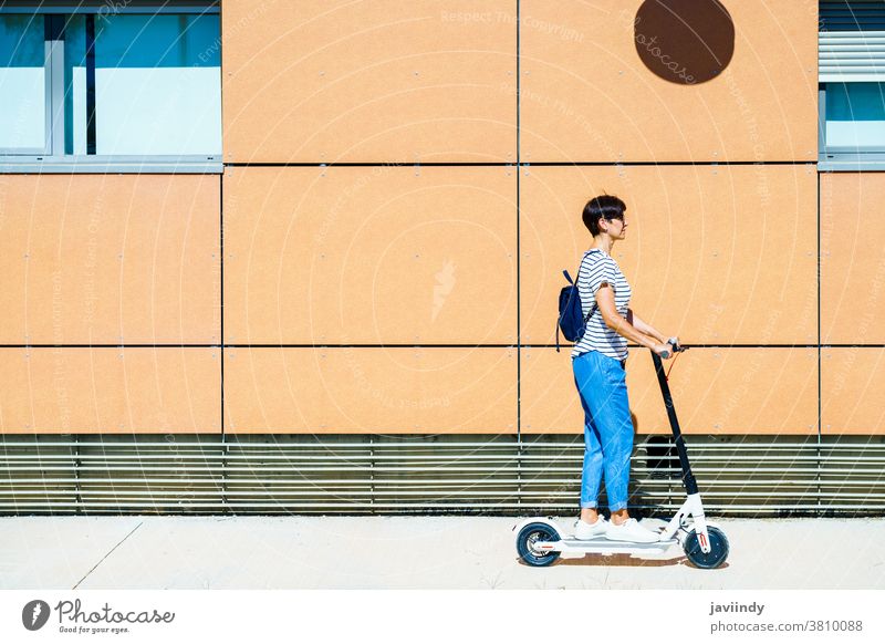 Woman riding around town on an electric scooter woman girl eco transportation urban lifestyle modern leisure city ride middle age female young active smile bike