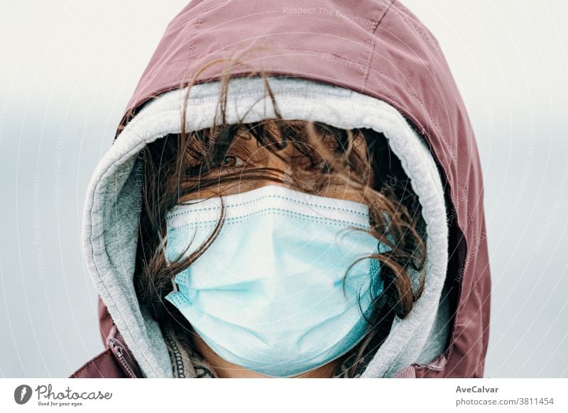 Close up of a woman face with the mask put on and the hair flying by the wind while wearing hiking clothes and looking straight to camera novel operating ill